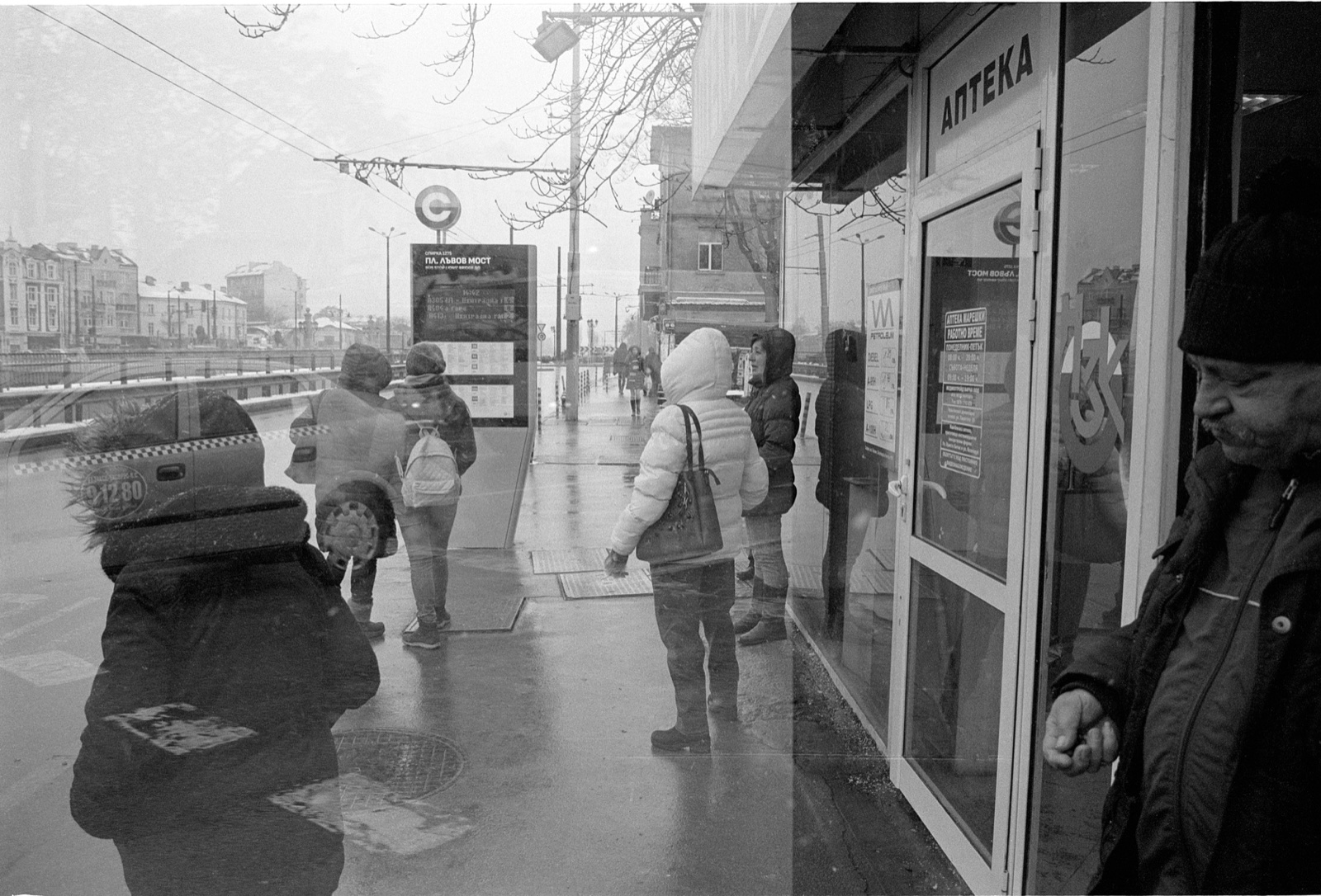 Black and white street photograph showing pedestrians and reflections on a rainy street in Sofia